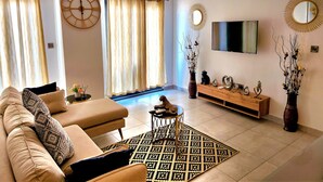 A living room with a sofa, coffee table, TV, decorative mirrors, and a large window with curtains.