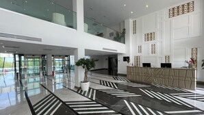 Un moderno vestíbulo de hotel con un ascensor de vidrio, una recepción y una planta grande en maceta.