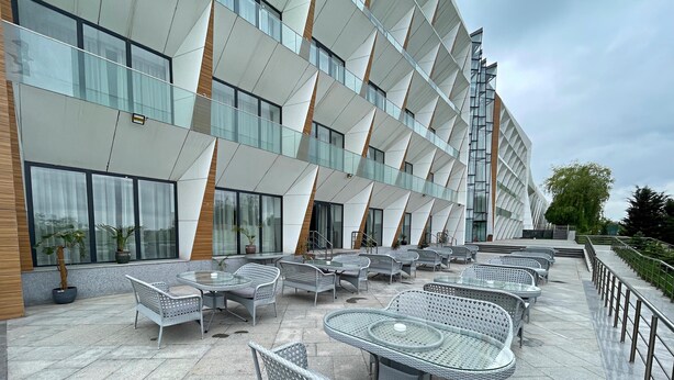 Un área de estar al aire libre con mobiliario de mimbre y un edificio moderno al fondo.