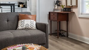 Un soggiorno moderno con un divano grigio, un tavolino da caffè con riviste, un tavolino laterale in legno e una cucina sullo sfondo.