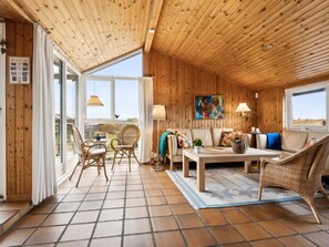 Een gezellig interieur van een chalet met houten wanden, een bank, een bijzettafeltje en rieten stoelen.