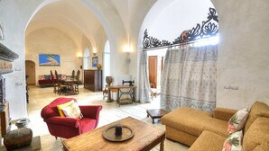 Un vaste espace de vie doté d’une cheminée, d’un fauteuil rouge et d’un canapé. Au fond, on aperçoit un coin repas avec une table et des chaises.