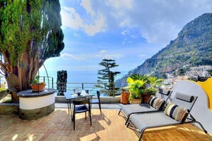 Una terraza con mesa y sillas, plantas en macetas y vistas al mar y a las montañas.