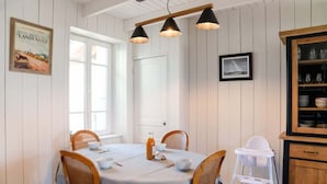Un comedor con una mesa redonda, sillas e iluminación colgante. Hay una pizarra, un cuadro enmarcado y un armario con cristalería.