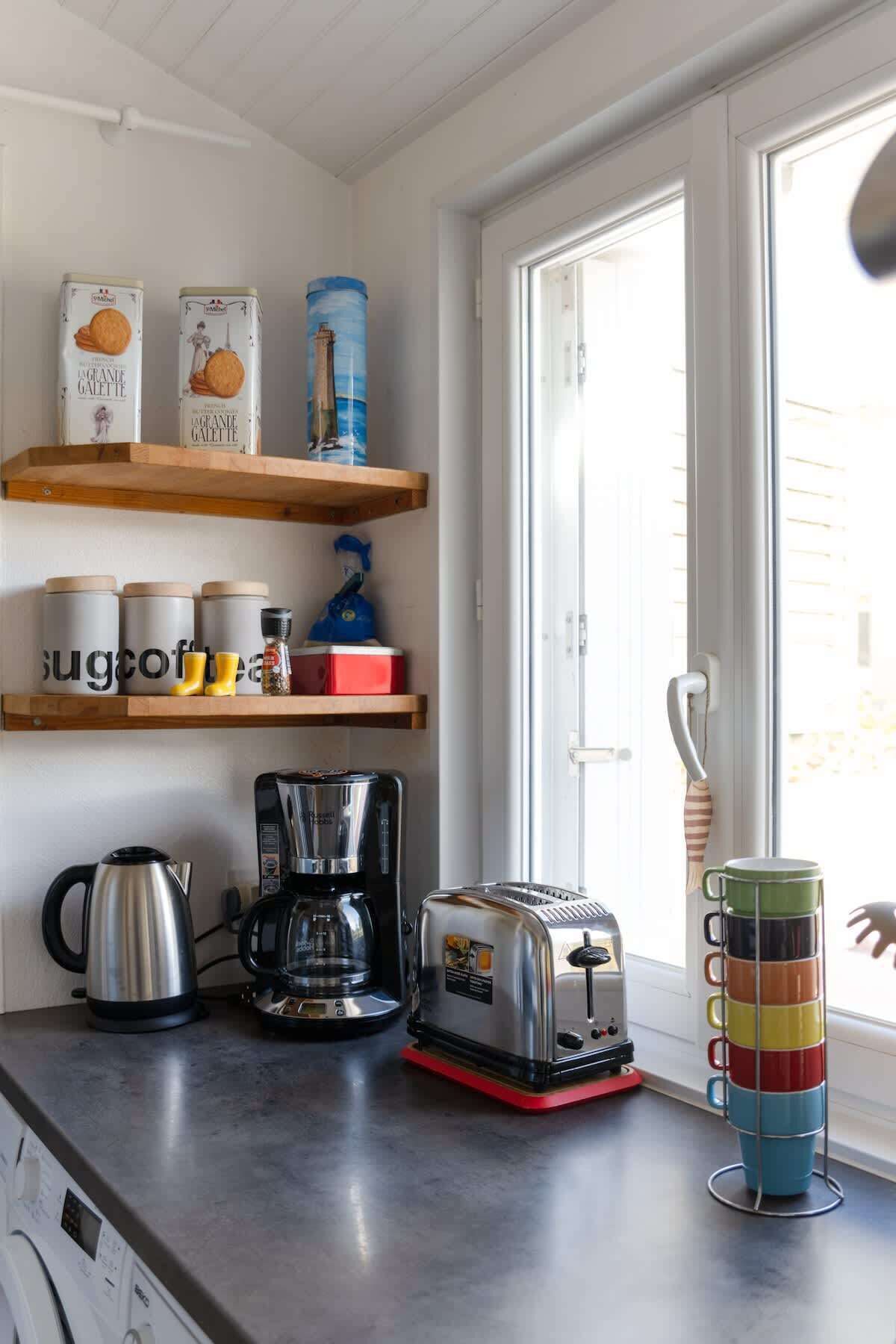 Eine Küche mit Kaffeemaschine, Toaster, Wasserkocher und einer Tassehalterung am Fenster.