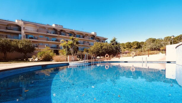 A swimming pool with clear blue water, surrounded by a building with multiple balconies and a clear sky. - Residencial Golden Beach by Interhome (St Carles de la Ràpita)