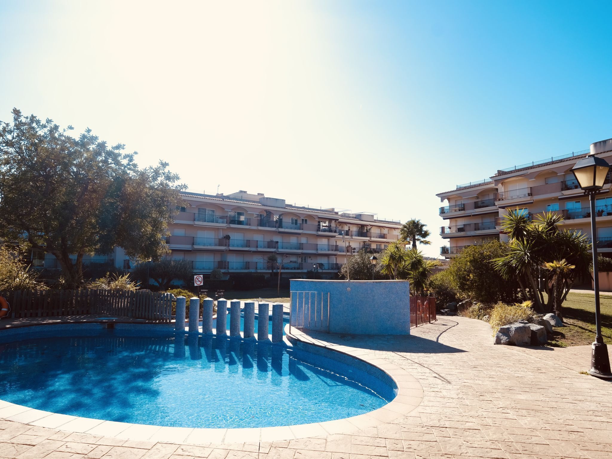Una piscina circondata da un solarium piastrellato, con un edificio sullo sfondo.