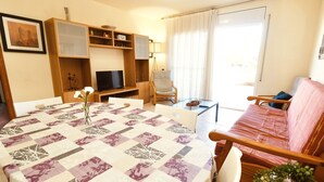 A cozy living room with a round table, a sofa, a TV, and a bookshelf. - Residencial Golden Beach by Interhome (St Carles de la Ràpita)