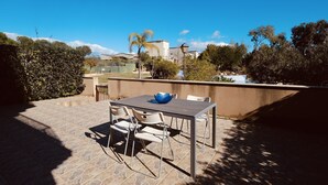 An outdoor patio with a table and chairs, a blue bowl, and a view of a residential area with trees and buildings. - Residencial Golden Beach by Interhome (St Carles de la Ràpita)