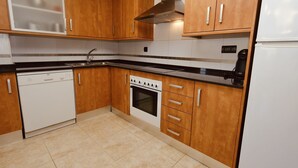 A kitchen with wooden cabinets, a built-in oven, a dishwasher, and a stainless steel range hood. - Residencial Golden Beach by Interhome (St Carles de la Ràpita)