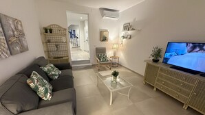 A modern living room with a grey sofa, a glass coffee table, a television, and a wicker sideboard.
