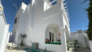 A white building with a pool, outdoor seating, and a clear blue sky.