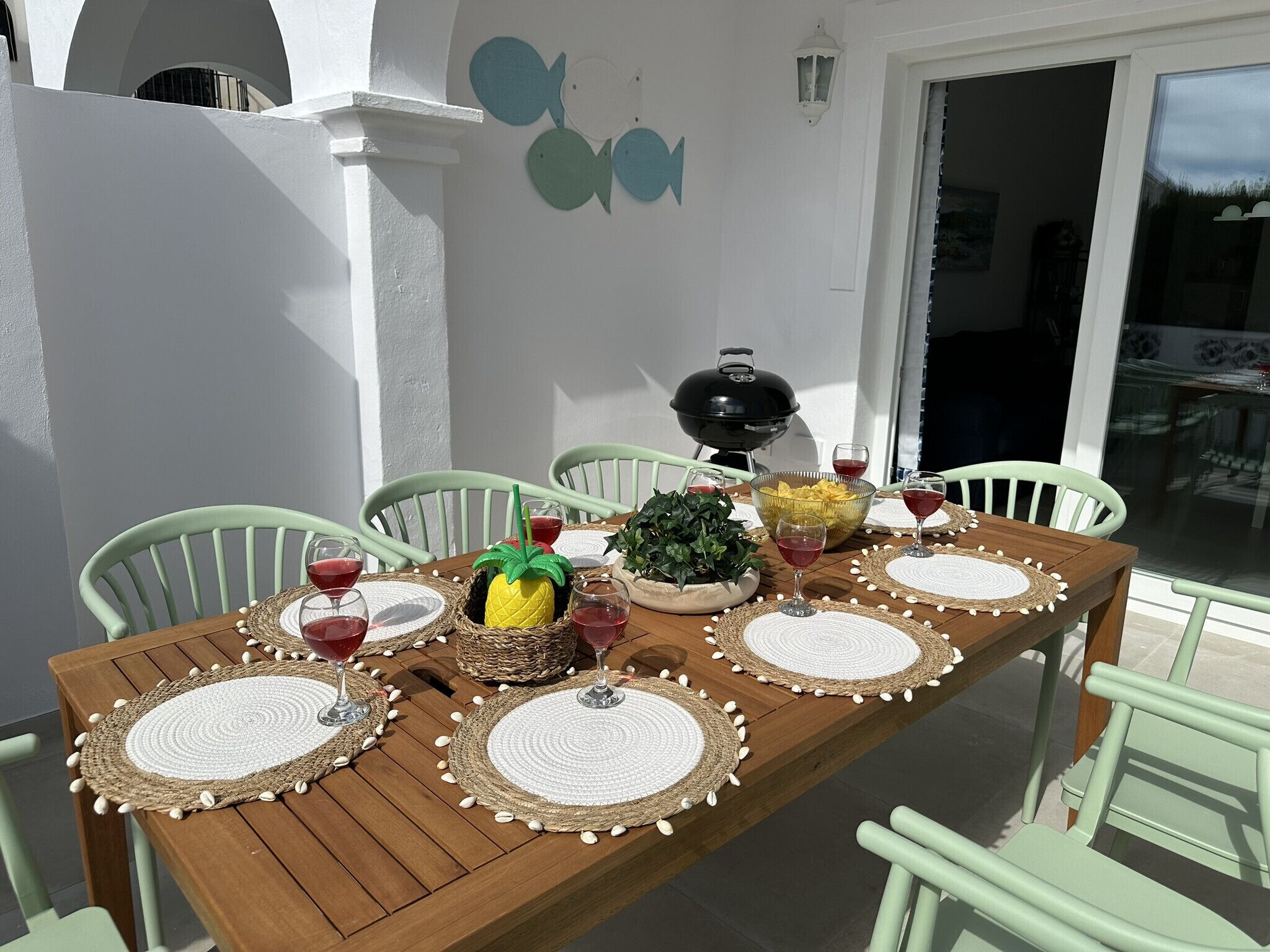 Ein Holzespeisetisch ist mit Platzsets, Weingläsern und einer Ananas als Mittelstück gedeckt.