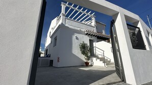 Un bâtiment blanc avec une entrée couverte, un pot de fleurs et un escalier menant à un balcon.