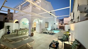 Une cour avec une piscine, des chaises longues et un espace repas comprenant une table et des chaises.