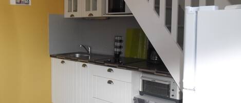 A compact kitchen with white cabinets, a microwave, a coffee maker, and a refrigerator.