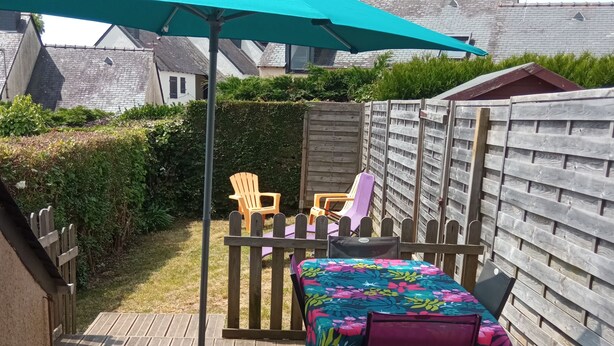 A wooden deck with a table and chairs, a blue umbrella, and a wooden fence.