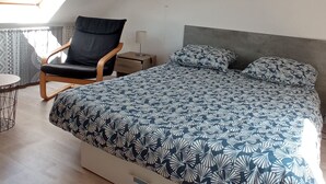 A bedroom with a bed, a chair, a small table, and a skylight.