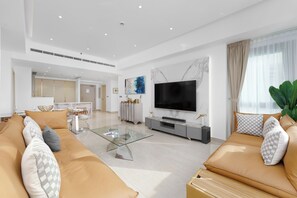 A spacious living room with a large TV, a glass coffee table, and a sofa set. - Maison Privee - High-End Palm Apt w/ Picturesque Seafront Views (Dubai)