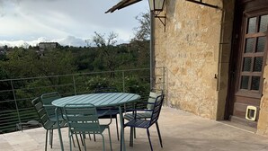A patio with a round table and chairs, a stone floor, and a view of a mountainous landscape.