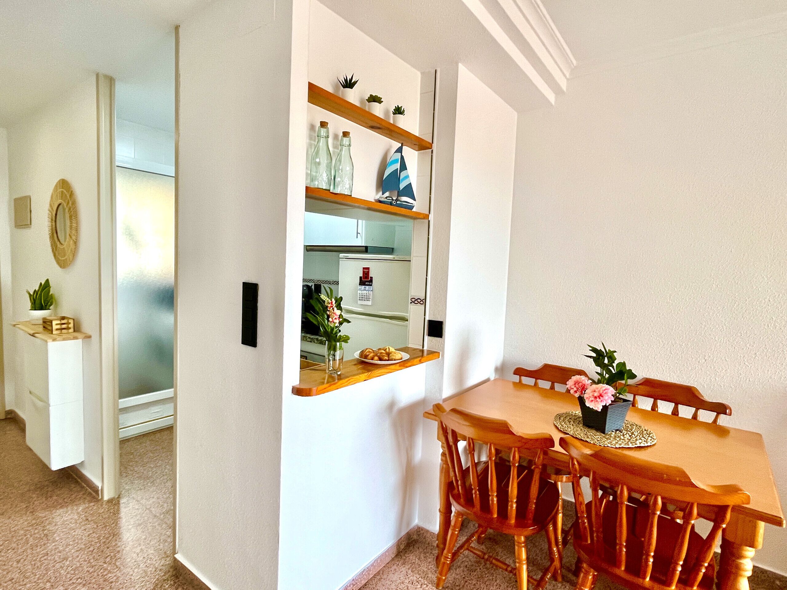 Ein Essbereich mit einem Holztisch und Stühlen, einer Vase mit Blumen sowie einem Regal mit Dekoration.