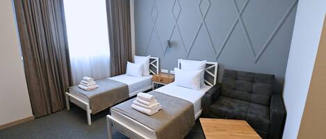 A hotel room with two single beds, a sofa, a wooden table, and a wall with geometric patterns.