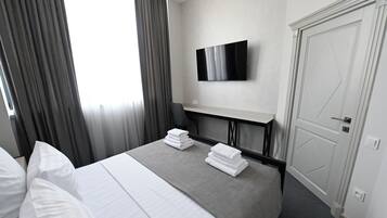 Habitación de hotel con cama, televisor de pantalla plana en la pared, puerta y ventana con cortinas.