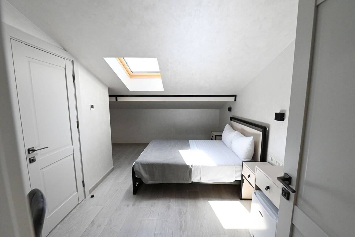 Une petite chambre à coucher moderne, dotée d’une lucarne, d’un lit, d’une table de chevet et d’une armoire.