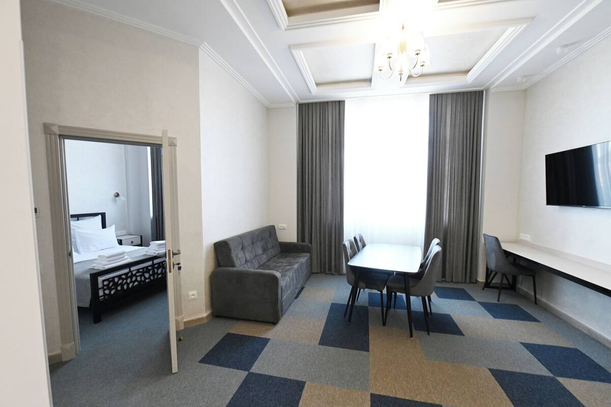 Une chambre d’hôtel comprenant un lit, un canapé, une table à manger avec des chaises, un téléviseur et un lustre.