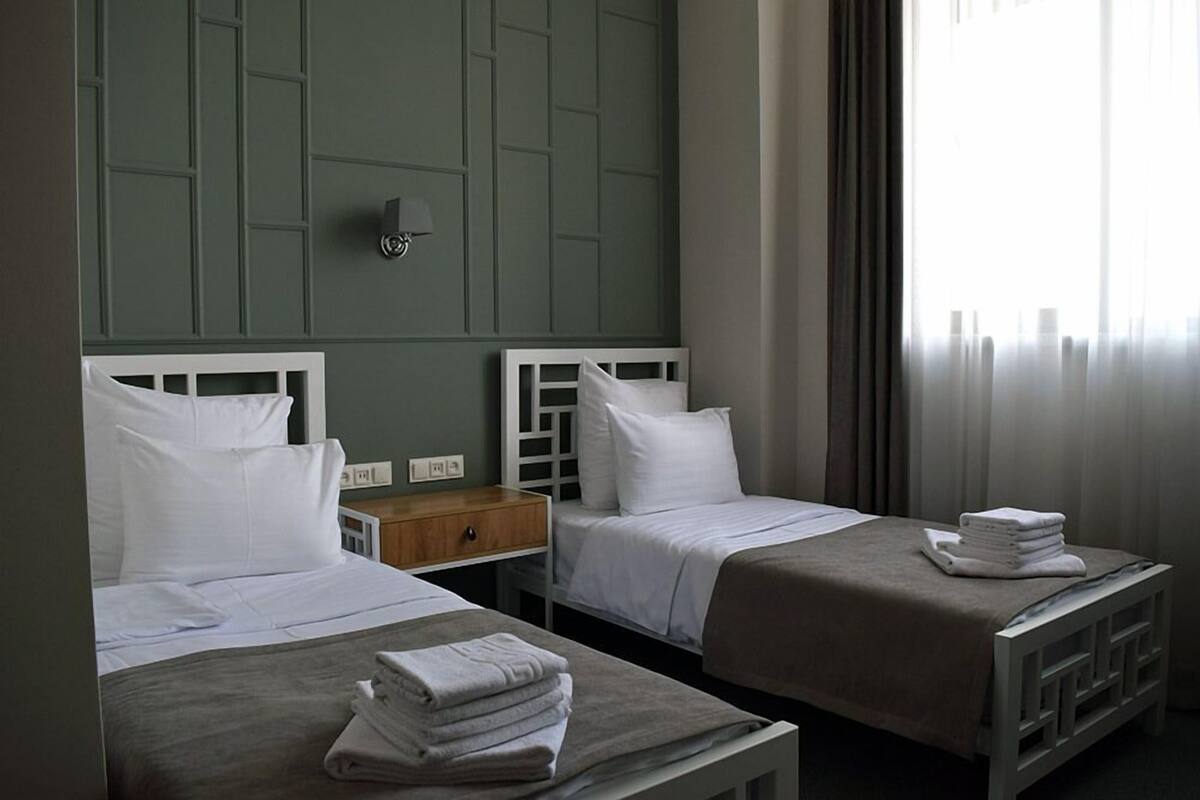 Une chambre d’hôtel avec deux lits, une table de chevet et une fenêtre avec des rideaux.