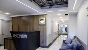 Et hotellets receptionområde med receptionsdisk, skilt med hotellets navn, en receptionsdisk og en blå sofa, samt en gang der fører til andre værelser.