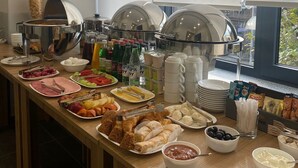 En buffet med forskellige spiser og drikkevarer, herunder frugt, kød og bagværk, anrettet på et træbord.