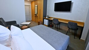 Et hotelværelse med en seng, to stole, et skrivebord, et fjernsyn og et lille tekøkken.