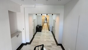 En moderne hotelgang med marmorgulv, hvide vægge og en trappe i midten, der fører op til en etage.