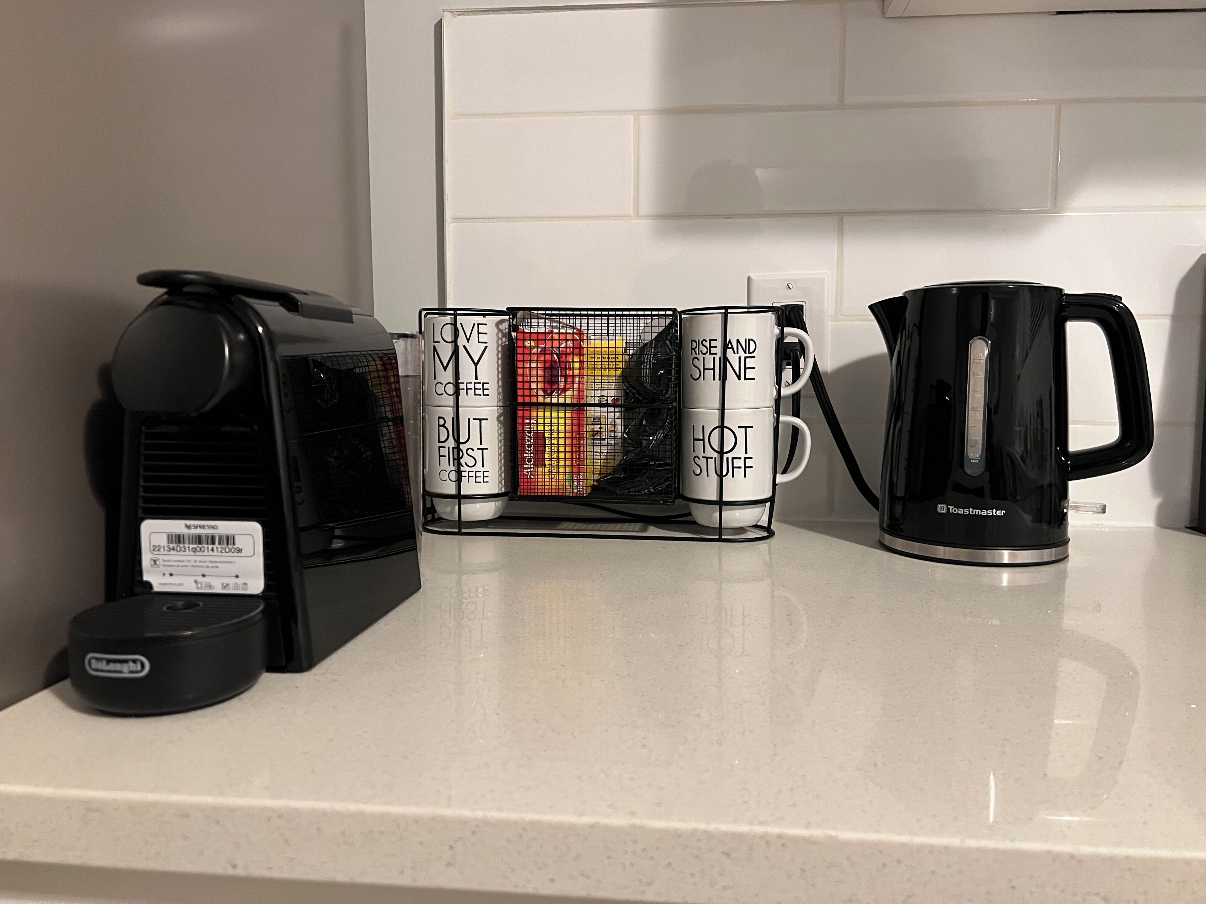 A kitchen counter with a coffee maker, a stack of mugs, and a kettle.