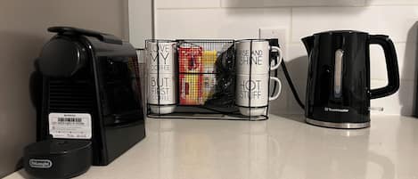 A kitchen counter with a coffee maker, a stack of mugs, and a kettle.