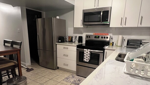 A modern kitchen with stainless steel appliances, white cabinetry, and a marble countertop.