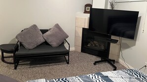 A room with a black sofa, a flat-screen TV, and a fireplace.
