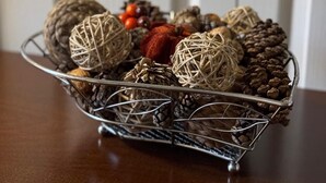A metal basket filled with decorative items like pinecones, pine needles, and a small pumpkin, placed on a wooden table.