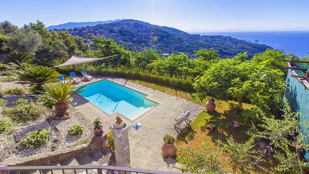 Una piscina rodeada de exuberante vegetación y una vista panorámica del mar y las colinas.