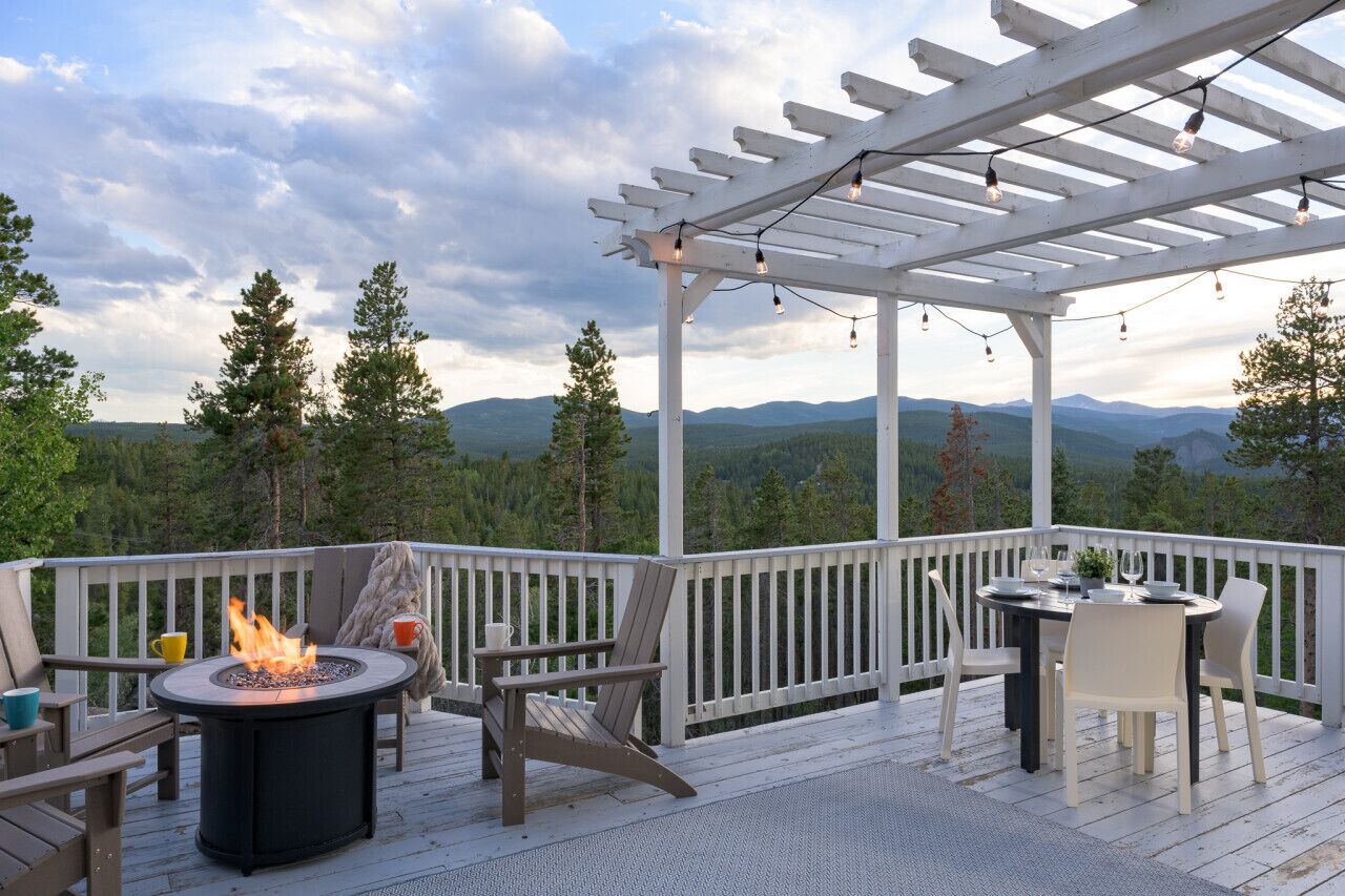 En terrasse med bålsted, udendørs møbler og en pergola med lyskæder.