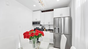 Una cucina moderna con mobili bianchi, elettrodomestici in acciaio inossidabile e un tavolo da pranzo in vetro con un vaso di rose rosse.