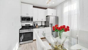 Una cucina moderna con mobili bianchi, elettrodomestici in acciaio inossidabile e un tavolo da pranzo in vetro abbinato a sedie bianche.