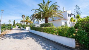 A residential street lined with white houses, palm trees, and a clear blue sky.