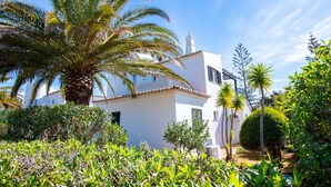 A white building with a tiled roof, surrounded by lush greenery and palm trees.