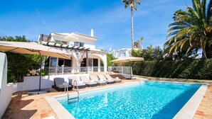 A poolside area with a clear blue pool, lounge chairs, and umbrellas.