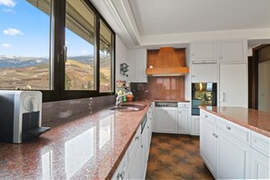 Une cuisine dotée d’une grande fenêtre, d’une machine à expresso intégrée et offrant une vue sur la campagne.