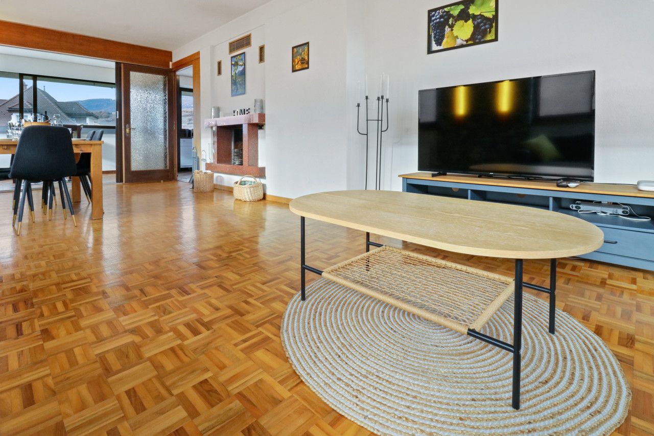 Ein modernes Wohnzimmer mit Holzboden, einem runden Tisch, einem Flachbildfernseher und einem Kamin.