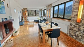 Ein Essbereich mit Holztisch, gedeckt für vier Personen, umgeben von Stühlen, mit einer Steinsäule und großen Fenstern mit Bergblick.
