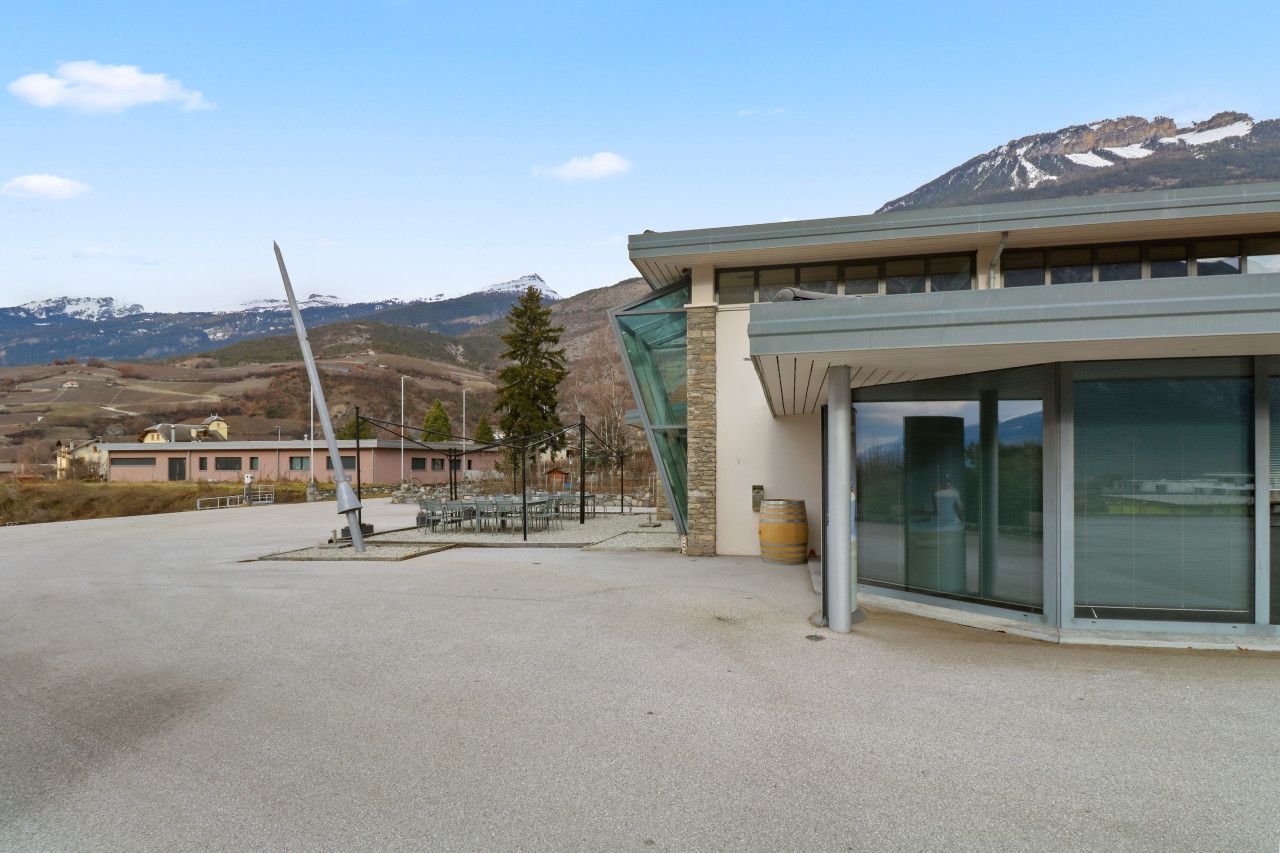 A modern building with a large glass facade, a wind turbine in the background, and a mountainous landscape.